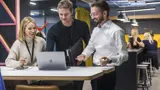 Two men and a woman stood up looking at a laptop